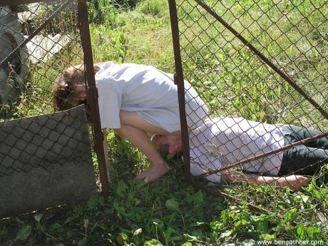 Caucasian lady GF broad straddles a boy BF man face outside of a doghouse in a yard - #173038